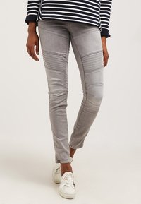 Jeans de mezclilla gris con detalles acanalados en los muslos, ajuste tapered y un ligero desvanecimiento. Combinados con zapatillas blancas para un contraste.