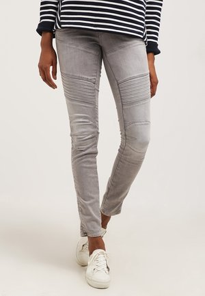 Jeans de mezclilla gris con detalles acanalados en los muslos, ajuste tapered y un ligero desvanecimiento. Combinados con zapatillas blancas para un contraste.