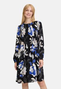Blumenkleid mit langen Ärmeln, schwarzer Grundfarbe, verziert mit blauen, weißen und beigen Blumen. Faltentextur und lockere Passform.