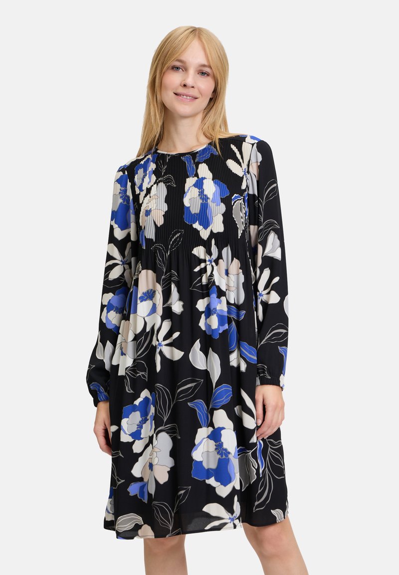 Blumenkleid mit langen Ärmeln, schwarzer Grundfarbe, verziert mit blauen, weißen und beigen Blumen. Faltentextur und lockere Passform.