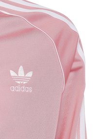 Hellrosa Adidas Trainingsjacke mit weißen Streifen, strukturiertem Stoff, geripptem Kragen und gesticktem Logo auf der Brust.