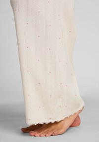 Ύφασμα εκρού με υφασμένο σχέδιο και μικρά ροζ μοτίβα καρδιάς. Δαντέλα στο τελείωμα. Ορατό πόδι, που αναδεικνύει το υλικό και το σχέδιο.