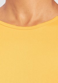 Gelbes geripptes Top mit rundem Ausschnitt, das eine glatte Textur und eine figurbetonte Passform aufweist, und das dehnbare sowie leichte Material betont.