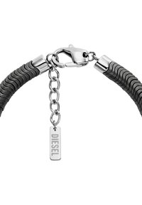 Bracciale in gomma nera con una texture rigata, dotato di una chiusura in metallo argentato e di una catena con un'etichetta rettangolare che riporta la scritta "DIESEL."