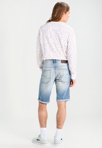 Camicia bianca a maniche lunghe con motivo di coriandoli colorati, abbinata a pantaloni corti di denim blu con risvolti e tasche posteriori.