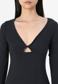 Svart langermet topp med ribbemønster, dyp V-hals og en nøkkelhulldetalj i midten. Stoffet ser ut til å være elastisk, med en figursydd silhuett.