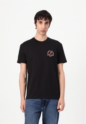 Black cotton t-shirt with a crew neck, featuring a small red and white logo on the chest, paired with blue denim jeans.