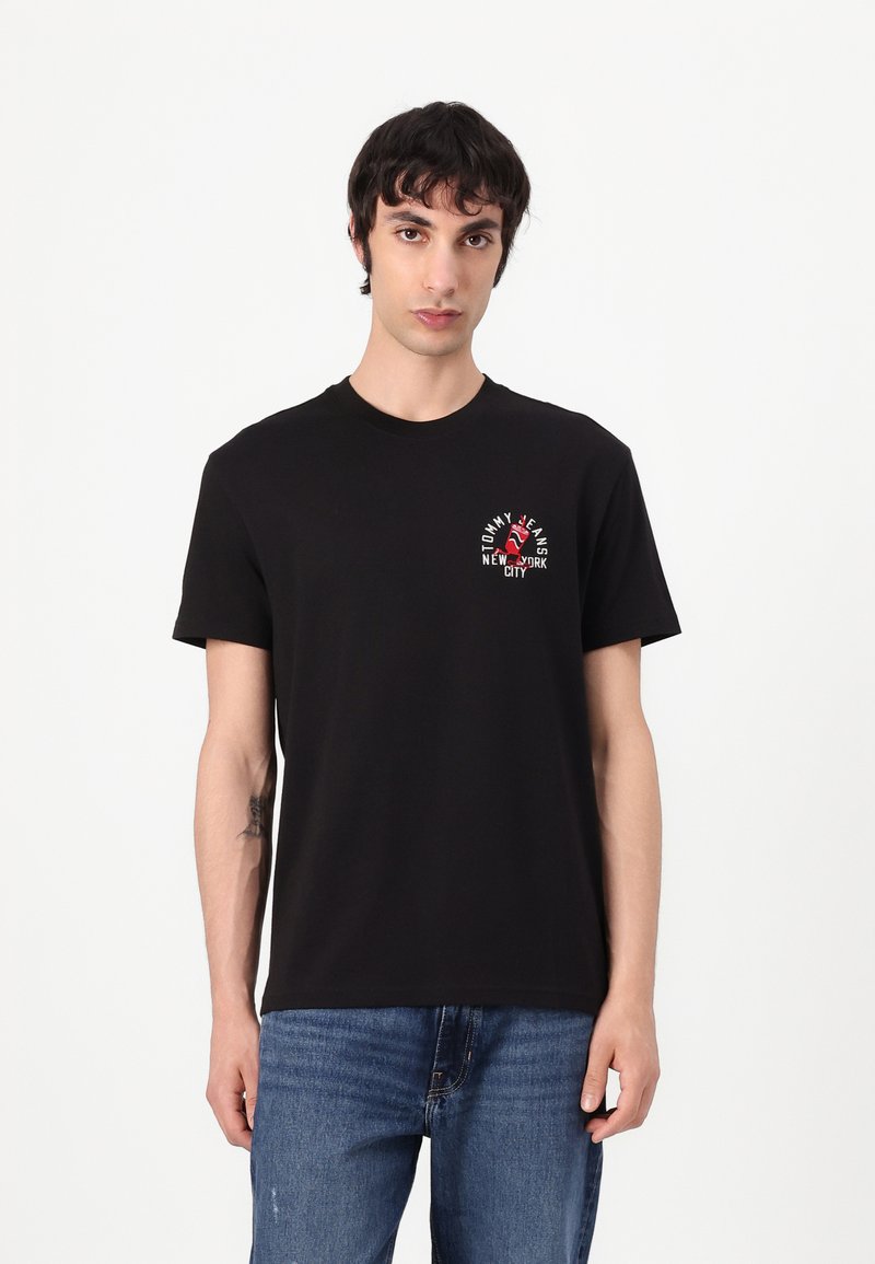 Black cotton t-shirt with a crew neck, featuring a small red and white logo on the chest, paired with blue denim jeans.