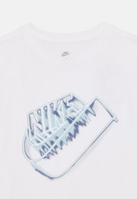 Λευκό μπλουζάκι με μεγάλο μπλε γραφικό του λογότυπου της Nike με σχεδιασμό σε σχήμα οδοντωτής λεπίδας, στρογγυλή λαιμόκοψη και κοντά μανίκια.