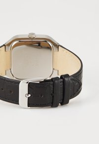 Μαύρη δερμάτινη ζώνη ρολογιού με υφή και ασημένια μεταλλική πόρπη. Τετράγωνη θήκη από ανοξείδωτο ατσάλι με γυαλιστερή φινίρισμα.