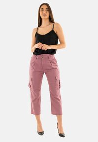 Pantalones cargo rosas con bolsillos frontales, diseño plisado y trabilla para cinturón. Combinados con una camiseta sin mangas negra con tirantes decorativos.