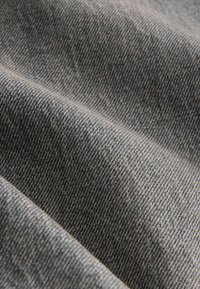 Zbliżenie na szarą tkaninę dżinsową ukazujące szczegółową teksturę splotu i naturalne fałdy.