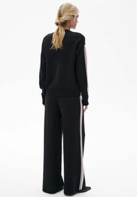 Czarny dzianinowy sweter i szerokie spodnie z jasnoszarymi bocznymi paskami, charakteryzujące się luźnym krojem i teksturowanym materiałem.