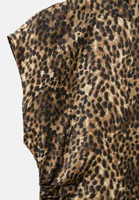 Tela de estampado de leopardo con manchas negras y marrones sobre un fondo marrón claro, que muestra el detalle de una prenda de manga corta.
