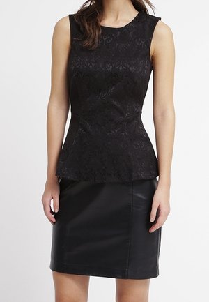 Ærmeløs sort peplumtop med subtilt blomsterprint kombineret med en ensfarvet sort knælængde nederdel på en stående kvinde.