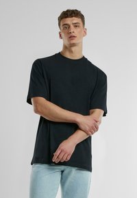 Černé tričko s krátkým rukávem a volným střihem, vyrobené z měkké bavlny. Klasický design s kulatým výstřihem, minimalistický styl bez viditelných vzorů.