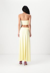Yellow two-piece garment featuring a fitted strapless top and long, flowing skirt. The fabric has a smooth texture, complemented by purple high heels.