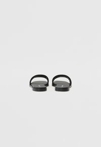 Sorte svarte sandaler med brede stropper, en glatt matte overflate og et minimalistisk design. Sålen har en liten bue for komfort.