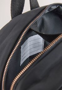 Intérieur d'un sac noir avec fermeture éclair ouverte montrant une étiquette blanche cousue comportant des lignes vierges pour le nom, l'e-mail et le téléphone.