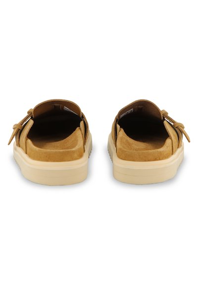 Καφέ σουέντ παπούτσια χωρίς κορδόνια με απαλό υφή και μπεζ λάστιχο σόλα, με λεπτομέρεια φιόγκου στο πλάι και ανοιχτή σχεδίαση στο πίσω μέρος.