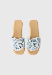 Light blue fabric slide sandals featuring a frayed flower accent, with a smooth beige insole and minimalistic design.