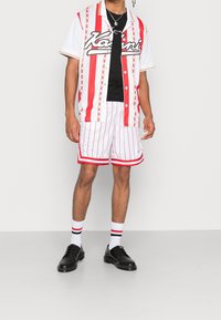 Camisa de manga corta con botones en rayas verticales rojas y blancas, combinada con shorts blancos con franjas rojas y zapatos negros.