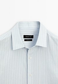 Lichtblauw gestreept overhemd met een klassieke kraag, zachte stof en witte knopen, met labels van Massimo Dutti en Made in China.