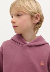 Roze katoenen hoodie met een kangoeroezak en oranje doodskop-en-botten borduursel op de linkerkant van de borst. Zachte textuur; casual pasvorm.