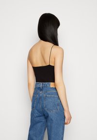 Débardeur noir côtelé à fines bretelles, associé à un jean denim bleu clair taille haute avec poches arrière et étiquette en cuir.