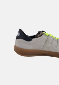 Sneaker in suede beige con tallone blu scuro, lacci verde neon e suola in gomma. Presenta un logo sul tallone e dettagli testurizzati.