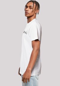 White cotton t-shirt with short sleeves, featuring a black graphic design on the front. The fit is relaxed, and the texture appears smooth.