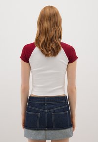 Top de manga corta con un cuerpo blanco y mangas burdeos, acompañado de una falda de mezclilla oscura con un dobladillo de mezclilla clara.