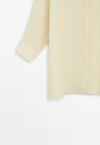 Long beige linen shirt sleeve and lower side with cuff, shown against a plain white background.