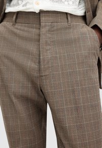 Hnědé kostkované kalhoty se směsí světlých a tmavých linií s jemnými oranžovými akcenty, vyrobené z texturované tkaniny. Design s plochým předním dílem.
