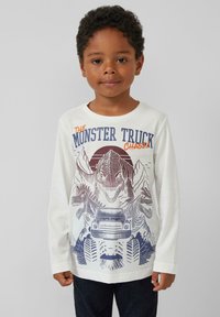 Weißes Langarmshirt mit einem Grafikdruck eines Dinosauriers und Monstertrucks in Blau und Orange. Runder Halsausschnitt und lässiger Schnitt. Dunkelblaue Jeans.