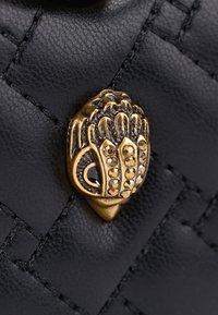 Czarna skórzana torba o plecionym wzorze, z złotym dekoracyjnym zapięciem w kształcie ręki z stylizowanymi wzorami i czarnymi kamieniami.