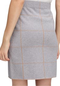 Jupe en tricot grise présentant un motif en grille avec des coutures marron clair. Elle a une coupe ajustée et une texture lisse.