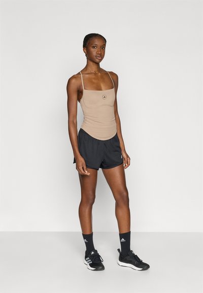 Top beige con spalline sottili e logo, abbinato a pantaloncini neri. Il tessuto è liscio e il design presenta una silhouette aderente.