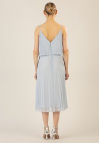 Hellblaues, gefaltetes Kleid mit V-Ausschnitt, dünnen Spaghettiträgern und fließendem Schnitt, kombiniert mit silbernen, hohen Sandalen.