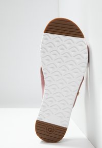 Shoe sole featuring white rubber material with textured grip pattern and brown accents. Sleek, rounded shape with brand logo.
