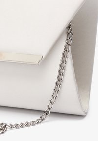 Bílá saténová kabelka s trojúhelníkovým klopou, stříbrnými kovovými detaily a kovovým řetízkovým popruhem. Hladká textura s minimalistickým designem.