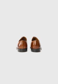 Zapatos de cuero marrón con un diseño elegante, punta redondeada y sutil detalle de costura. Las suelas negras ofrecen contraste y durabilidad.