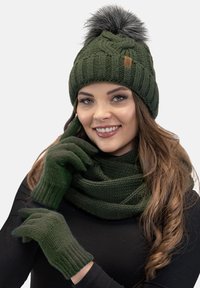Dark green knitted beanie with a faux fur pom-pom, matching dark green scarf, and gloves, featuring ribbed texture and a casual design.
