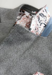 Grauer Blazer aus strukturiertem Stoff, mit einer Futter in blumigem Muster in sanften Farben und einem hellblauen Akzent am Kragen.
