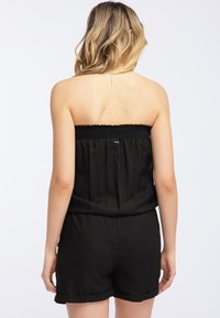 Mono negro sin tirantes con escote fruncido, cuerpo recogido y pantalones cortos con dobladillos doblados. Tejido suave y ligero.