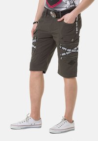 Cargo-Shorts aus olivgrünem Stoff, ausgestattet mit mehreren mit Reißverschluss verschlossenen Taschen, weißen Texthighlights und einem lässigen Schnitt. Gummierter Knopf-Detail.