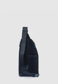 Borsa a tracolla navy con tessuto testurizzato, forma triangolare sottile, tracolla regolabile e dettagli con cerniere azzurro chiaro. Una tasca frontale visibile.