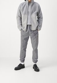 Grå fleecejacka med en slät panel, ribbade grå tröja under, grå cargo-byxor och svarta snörskor med en tjock sula.