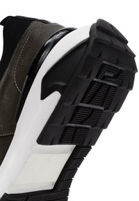 Sneaker z ciemnozielonym zamszowym wierzchem, czarnymi akcentami oraz grubą, textured gumową podeszwą, z widoczną białą podeszwą środkową i detalami zapewniającymi przyczepność.