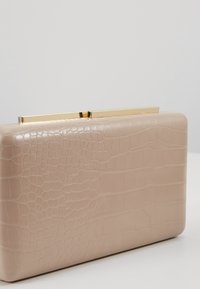 Sac pochette rectangulaire beige avec texture crocodile et fermoir métallique doré brillant sur le dessus, sur fond clair uni.
